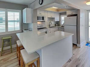 A modern kitchen with white cabinetry, a central island, a microwave, an oven, and a refrigerator. - Pointe South 207 | Stunning Views + Pool (Fort Myers Beach)