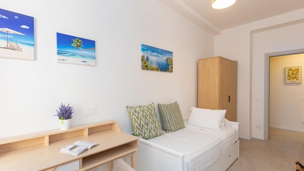 Een slaapkamer met een bed, een bureau, een stoel, een garderobe en twee wanddecoraties.
