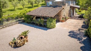Una casa de piedra con tejado de baldosas, rodeada por un camino de grava y abundante vegetación.