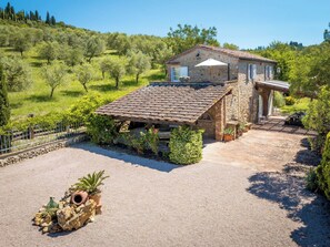 Un bâtiment en pierre, doté d’un toit en tuiles, entouré d’une allée gravillonnée et de verdure.