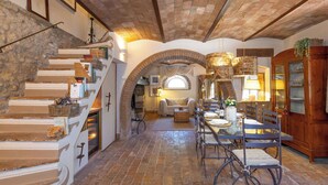 Un interior espacioso con una escalera de piedra, un comedor con una mesa larga y una zona de estar acogedora.