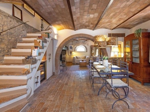 Un intérieur spacieux agrémenté d’un escalier en pierre, d’un coin repas avec une longue table et d’un espace salon confortable.