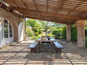 Eine Außenpatio mit einem Holztisch und Bänken, umgeben von Ziegelmauern und einem überdachten Bereich.