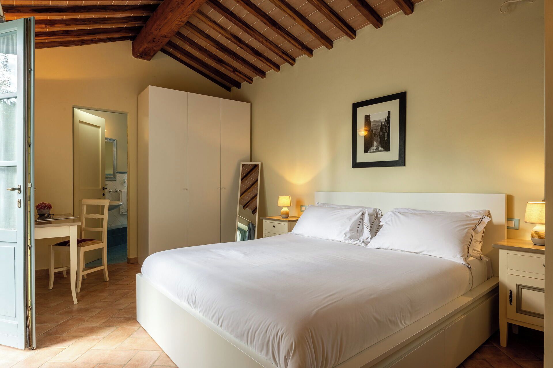 A bedroom with a large bed, bedside tables, a wardrobe, and a mirror.