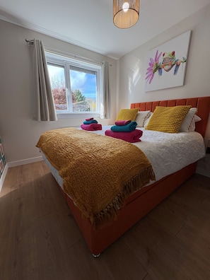 A bedroom with a bed, a window with curtains, a painting on the wall, and a wooden floor. - Stylish 2 bedroom Cottage Near Stirling + Parking & Pets (Stirling)