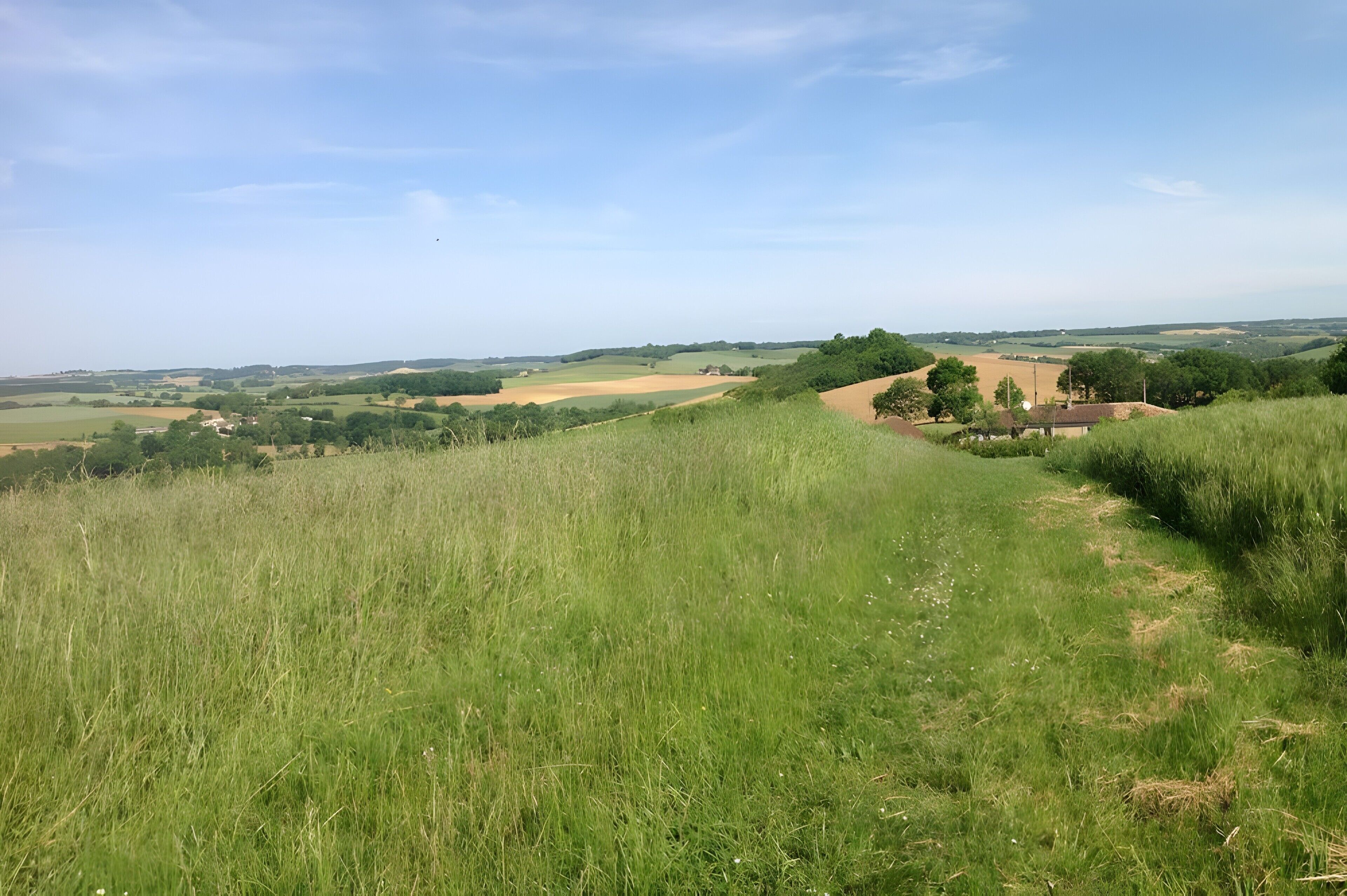 A rural landscape with rolling hills, a clear sky, and a distant view of a small village.