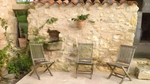 A stone wall with two wooden chairs and potted plants.
