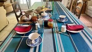 A dining table set with plates, bowls, and utensils, surrounded by chairs and a vase with flowers.