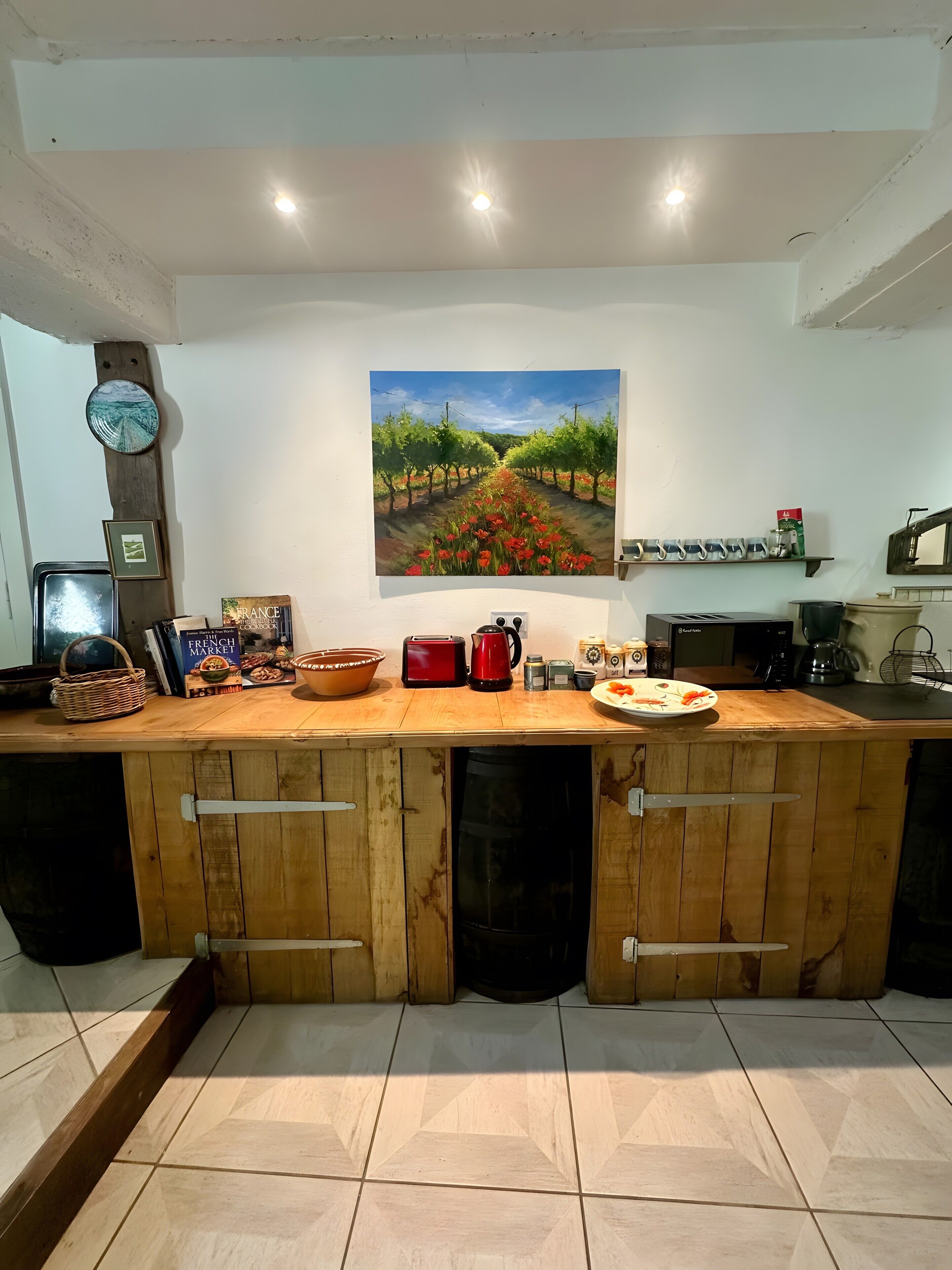 A kitchen with a wooden countertop, a painting of a vineyard, and various kitchen appliances.