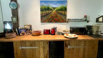 A kitchen with a wooden countertop, a painting of a vineyard, and various kitchen appliances.