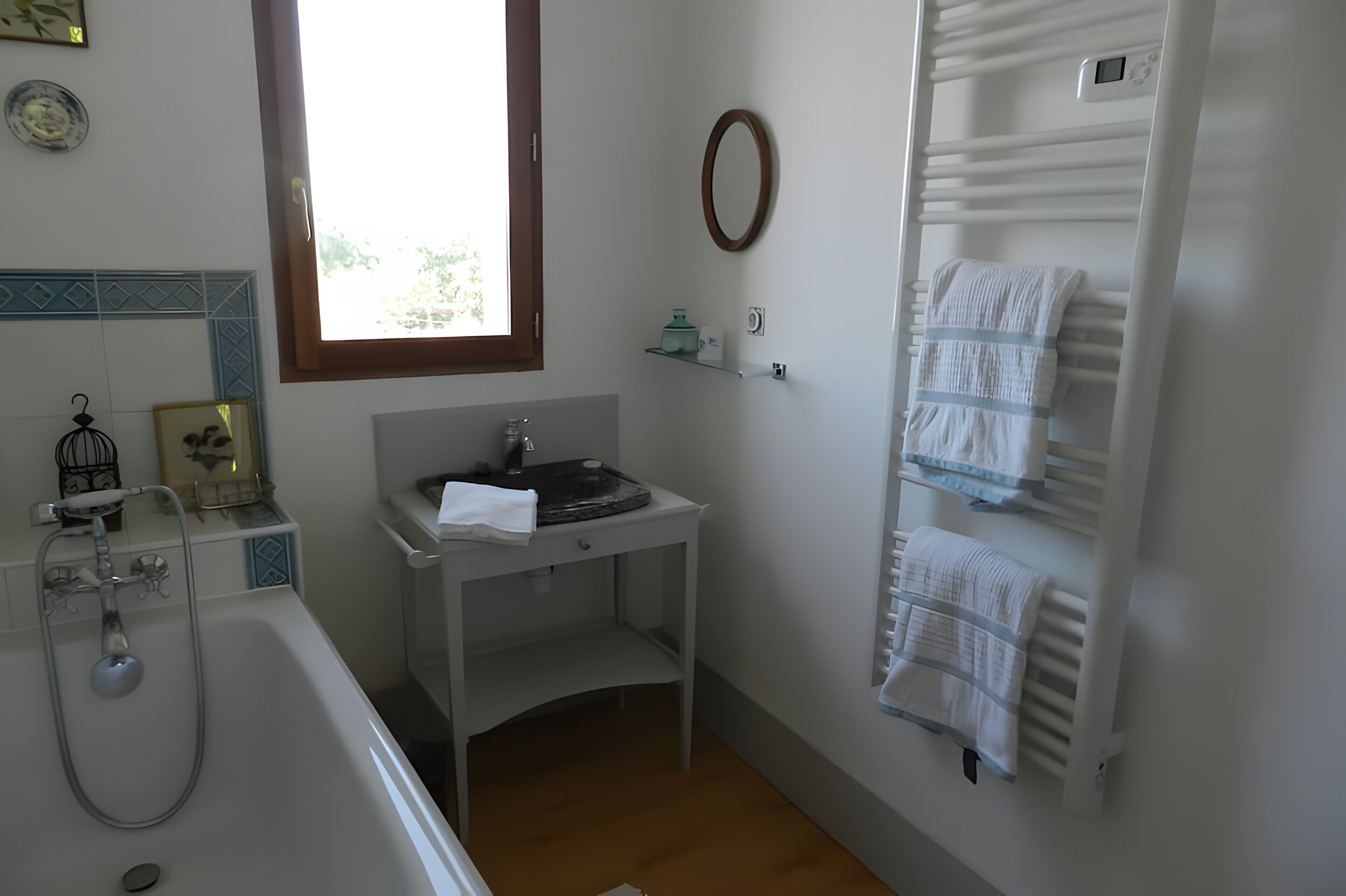 Ein Badezimmer mit Badewanne, Waschbecken inklusive Spiegel, Handtuchhalter und einem Fenster.
