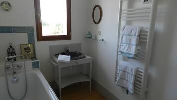 Ein Badezimmer mit Badewanne, Waschbecken inklusive Spiegel, Handtuchhalter und einem Fenster.