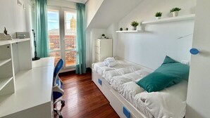A room with a bed, a desk, a chair, a window with curtains, and a view of buildings outside. - Apartment Ria de Ajo 12021 (Ajo)