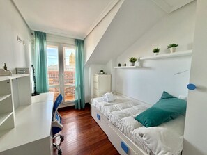 Ein Zimmer mit einem Bett, einem Schreibtisch, einem Sessel, einem Fenster mit Vorhängen und Blick auf Gebäude.