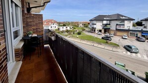 A balcony with a table and chairs, overlooking a street with parked cars and buildings. - Apartment Ria de Ajo 12021 (Ajo)