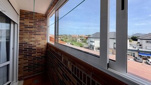 A balcony with brick walls, large windows, and a view of a residential area. - Apartment Ria de Ajo 12021 (Ajo)