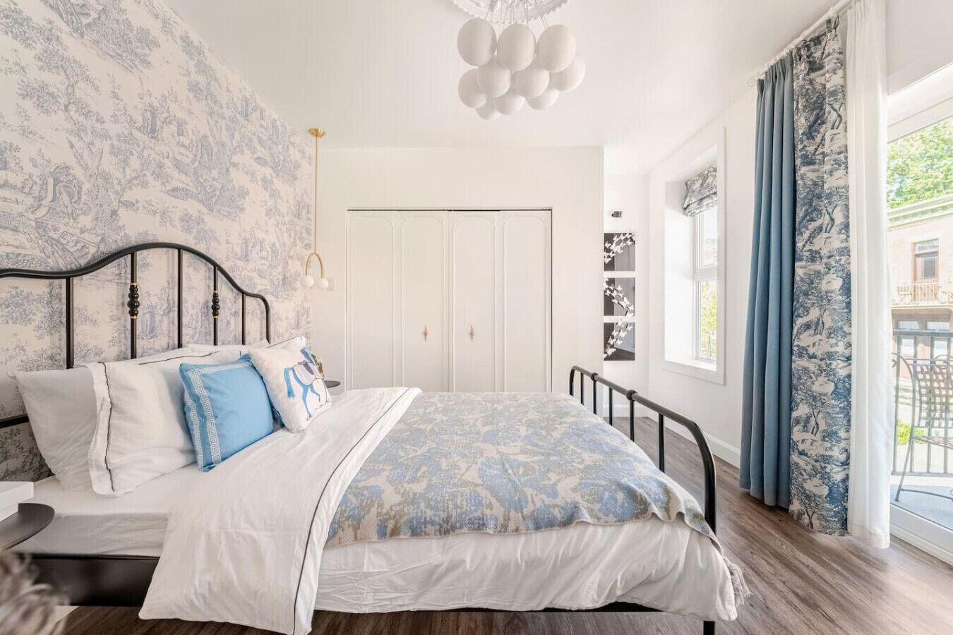 A bedroom with a bed, a wardrobe, a chandelier, and a view of the outside.