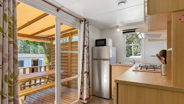 A kitchen with a refrigerator, microwave, and stove, a wooden bench outside, and a sliding glass door.