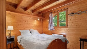 A wooden-paneled bedroom with a bed, bedside table, lamp, window, and radiator. - Apartment 'Lys blanc' with Mountain View, Wi-Fi and Air Conditioning (Vaulnaveys-le-Bas)