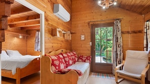 A wooden cabin interior with a bed, a sofa, a chair, and a door leading outside. - Apartment 'Lys blanc' with Mountain View, Wi-Fi and Air Conditioning (Vaulnaveys-le-Bas)