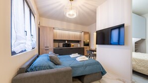 Un dormitorio moderno con cama, zona de estar, televisor y kitchenette.