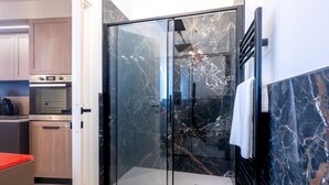 Una cocina moderna con electrodomésticos integrados, cabina de ducha con mampara de vidrio y suelo de mármol.