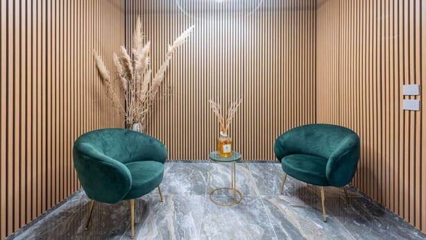 Un interior moderno con dos sillones tapizados en verde, una pequeña mesa redonda con un florero y una lámpara decorativa en el techo.