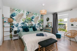 A bedroom with a bed, a bench, a chair, a dresser, a mirror, a window with a view, and a wall with a leaf pattern. - Zen Room Near Vannes (La Vraie-Croix)