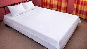 Een eenpersoonsbed met witte lakens, een zwart metalen frame en een rode muur.