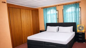 Een slaapkamer met een zwart bed, een houten garderobe en een nachtkastje met een ventilator.