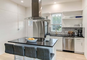 A modern kitchen with a central island, stainless steel appliances, and a window with blinds. - Eagles Nest View of Lake Buchanan - 2BR w Hot Tub & Gorgeous Views (Burnet)