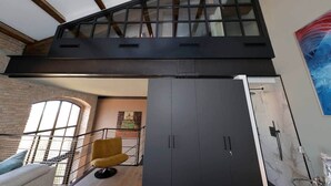 En modern inredning med högt tak, synliga träbjälkar, ett stort fönster, en gul stol och en vägg av marmor.