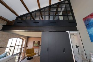 Ein modernes Interieur mit hoher Decke, freiliegenden Holzbalken, einem großen Fenster, einem gelben Sessel und einer Marmorwand.