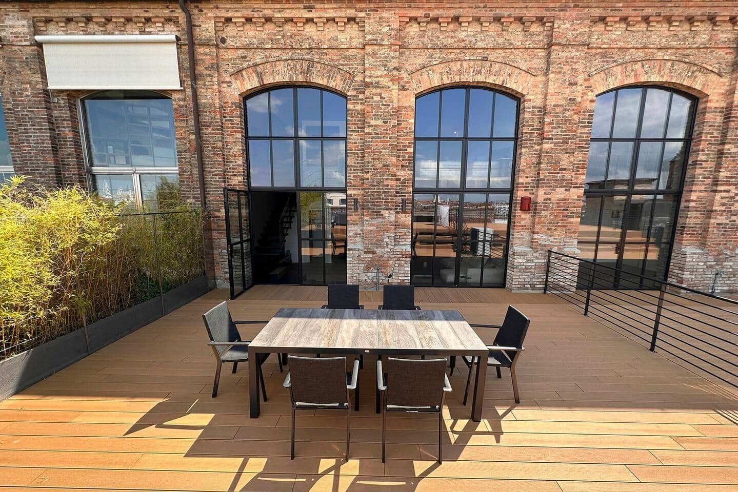 A brick building with large arched windows and a wooden deck with a table and chairs.