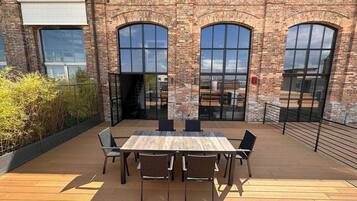 A brick building with large arched windows and a wooden deck with a table and chairs.