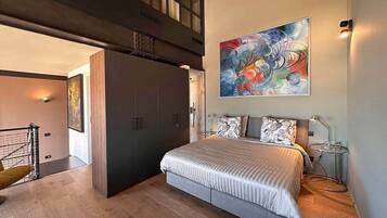 Ein Schlafzimmer mit einem Bett, einem großen abstrakten Gemälde, einem Schreibtisch mit Lampe und einer Treppe, die zu einer oberen Ebene führt.