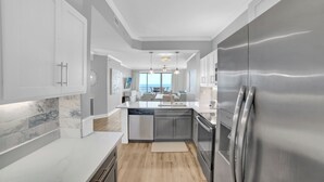 Eine moderne Küche mit Geschirrspüler, Edelstahlkühlschrank und Marmorfliesenspiegel.
