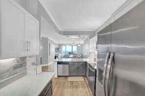 Eine moderne Küche mit Geschirrspüler, Edelstahlkühlschrank und Marmorfliesenspiegel.