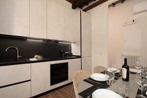 A modern kitchen with a black countertop, white cabinets, and a dining area with a table set for two. - San Niccolò Atelier Grande (Firenze)