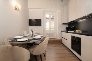 A modern kitchen with a dining area, a TV mounted on the wall, and a view through a glass door. - San Niccolò Atelier Grande (Firenze)