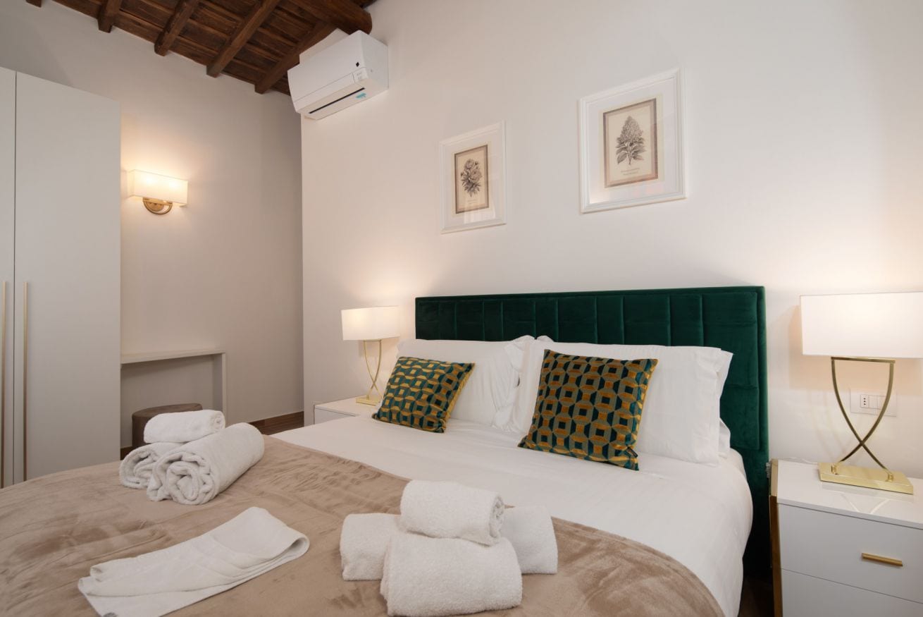 Ein Hotelzimmer mit einem Bett, zwei Nachttischen, einer Wand-Klimaanlage und zwei gerahmten Bildern.