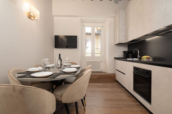A modern kitchen with a dining area, a TV mounted on the wall, and a view through a glass door. - San Niccolò Atelier Grande (Firenze)