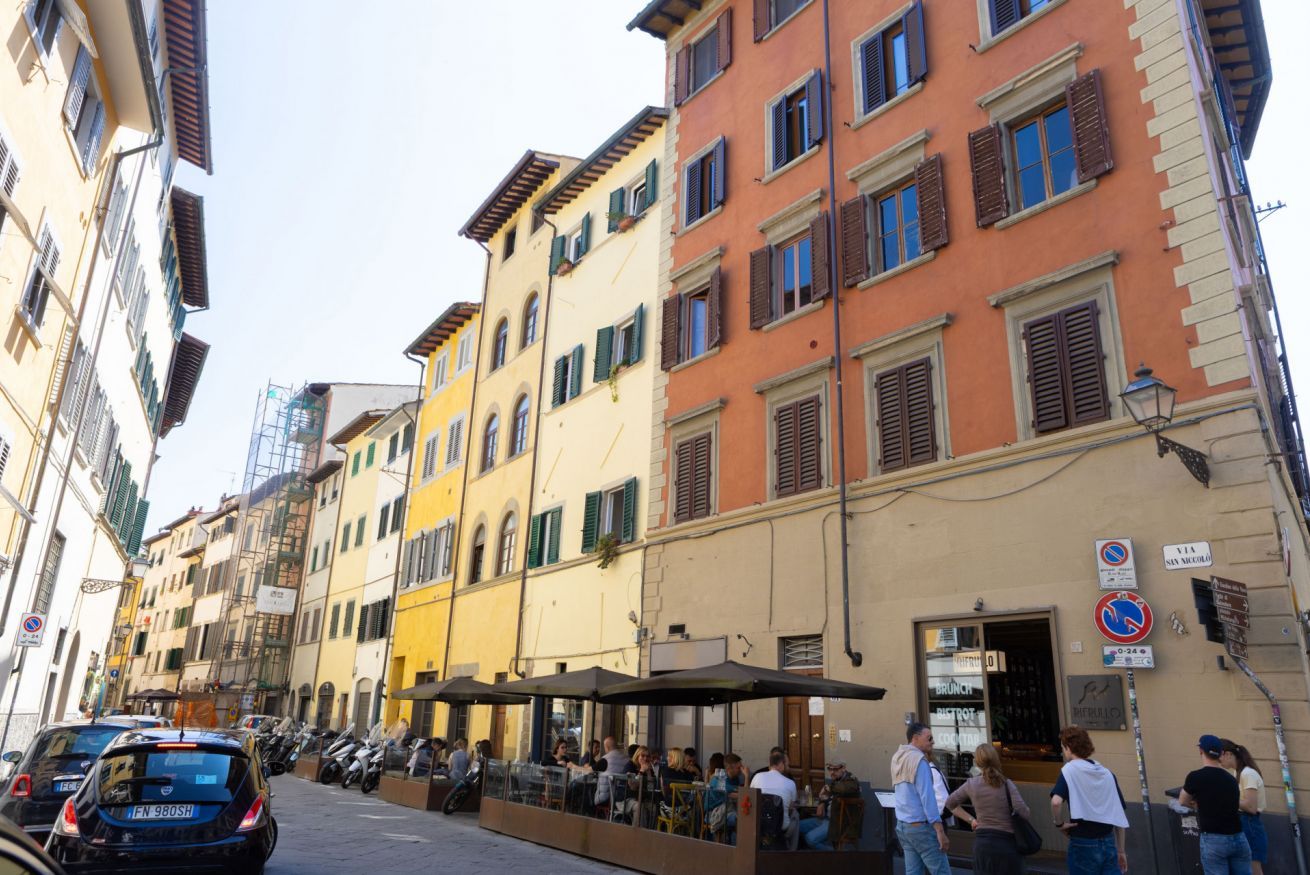 A street with colorful buildings, outdoor seating, and parked cars.