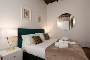 A neatly made bed with white linens, a green headboard, and a round mirror on the wall. - San Niccolò Atelier Grande (Firenze)