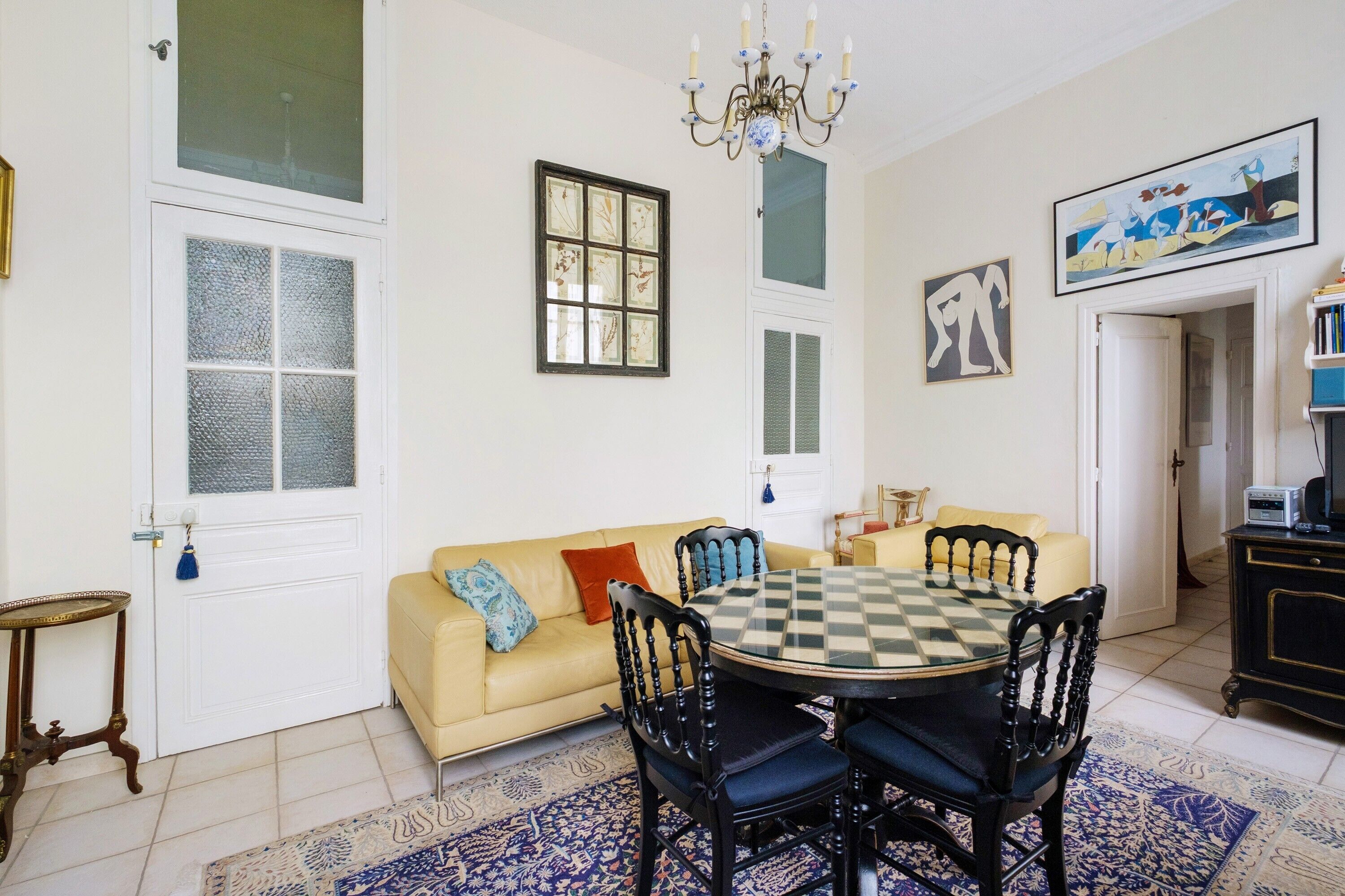 A dining area with a checkered table, chairs, a sofa, and a chandelier.
