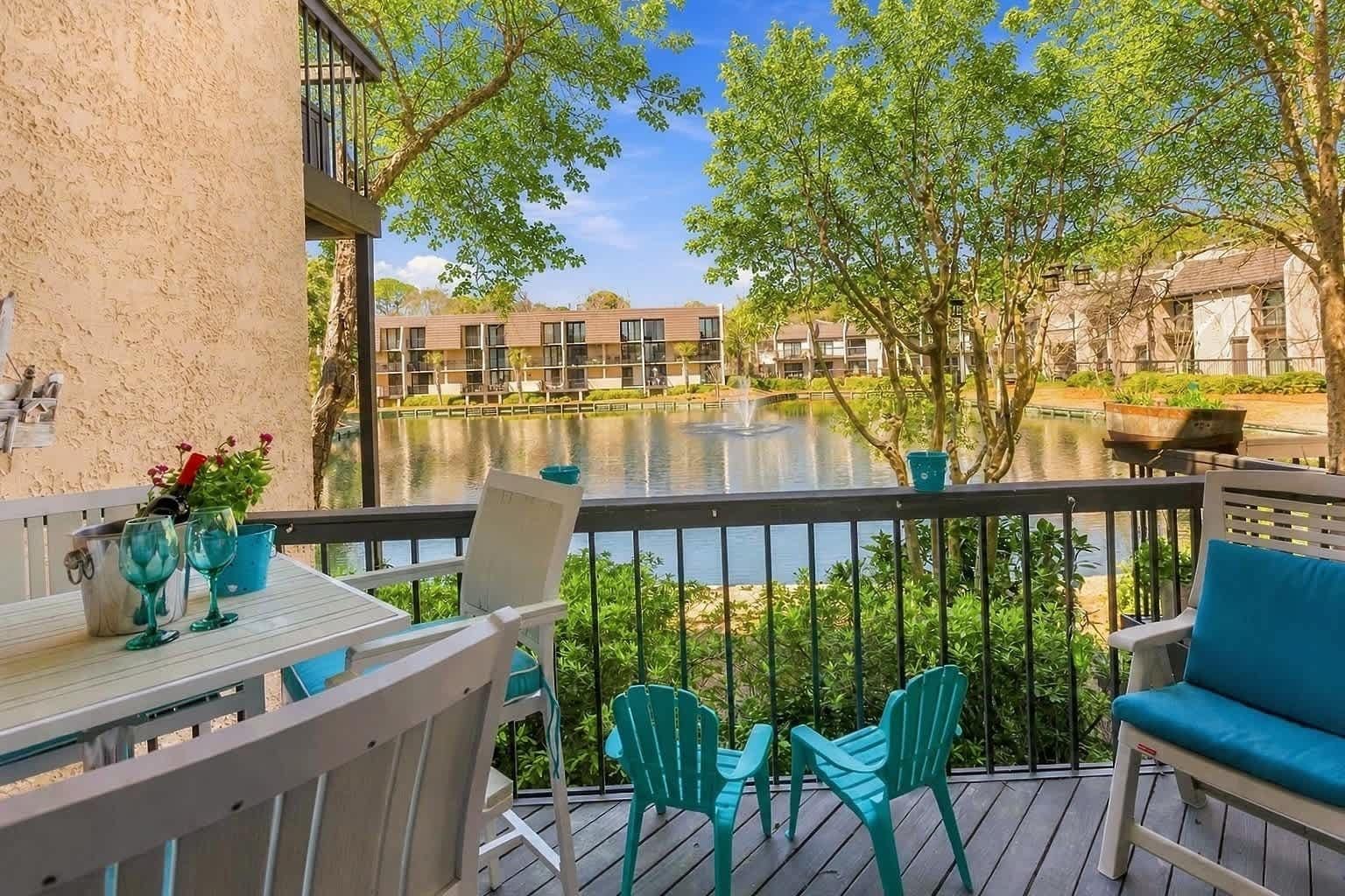 A balcony with a view of a lake, outdoor seating, and a building in the background.