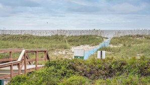 Pasarela de madera que conduce a una playa, con un letrero y un sendero azul.