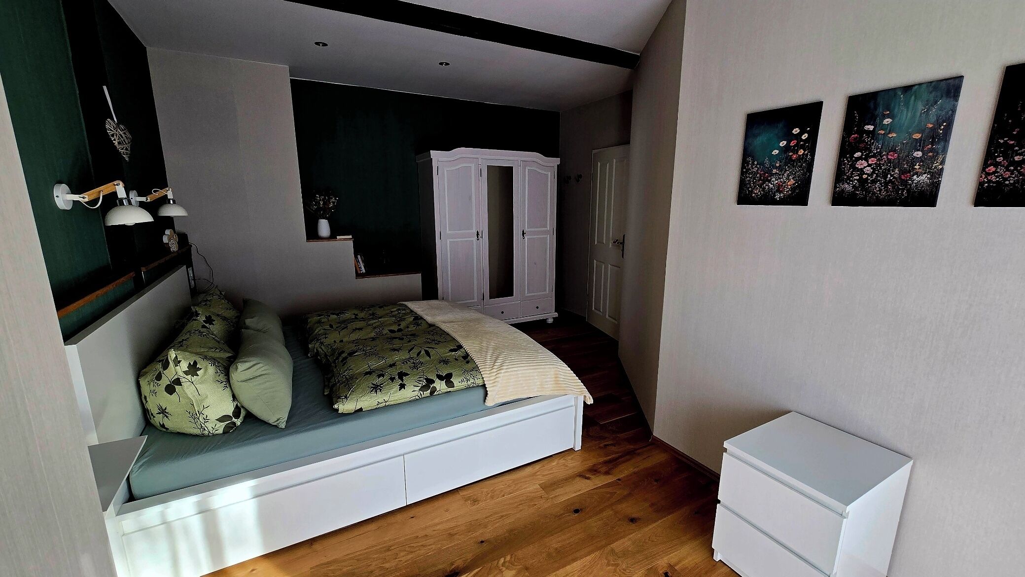 Een kleine kamer met een bed, een witte garderobe en een klein wit kastje.