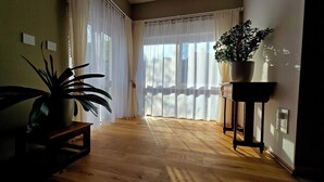 Une pièce avec un plancher en bois, une plante en pot, une petite table et une fenêtre ornée de rideaux légers.