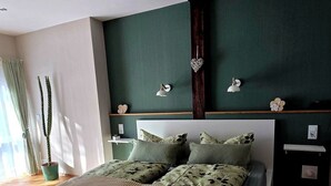 Une chambre moderne avec un plancher en bois, un lit recouvert d’une courtepointe à rayures vertes et beiges, et un mur d’accent de couleur vert foncé.